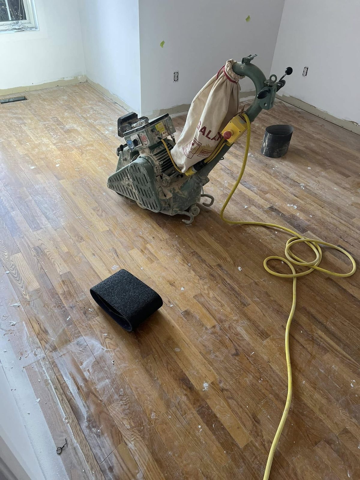 Sablage d'un plancher de bois franc en cours avec ponceuse professionnelle